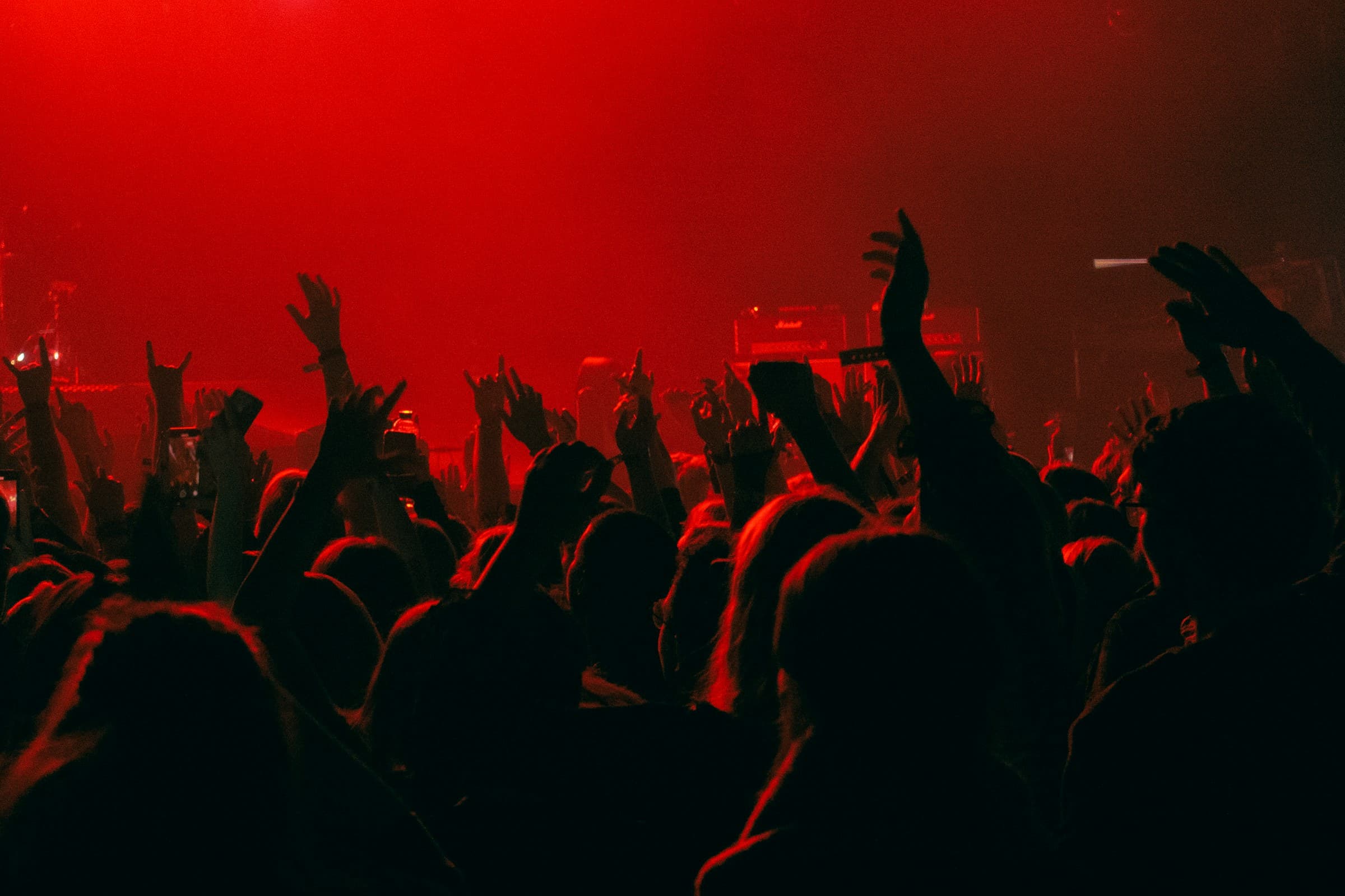 Multidão de show com as mãos erguidas, sob luz vermelha intensa